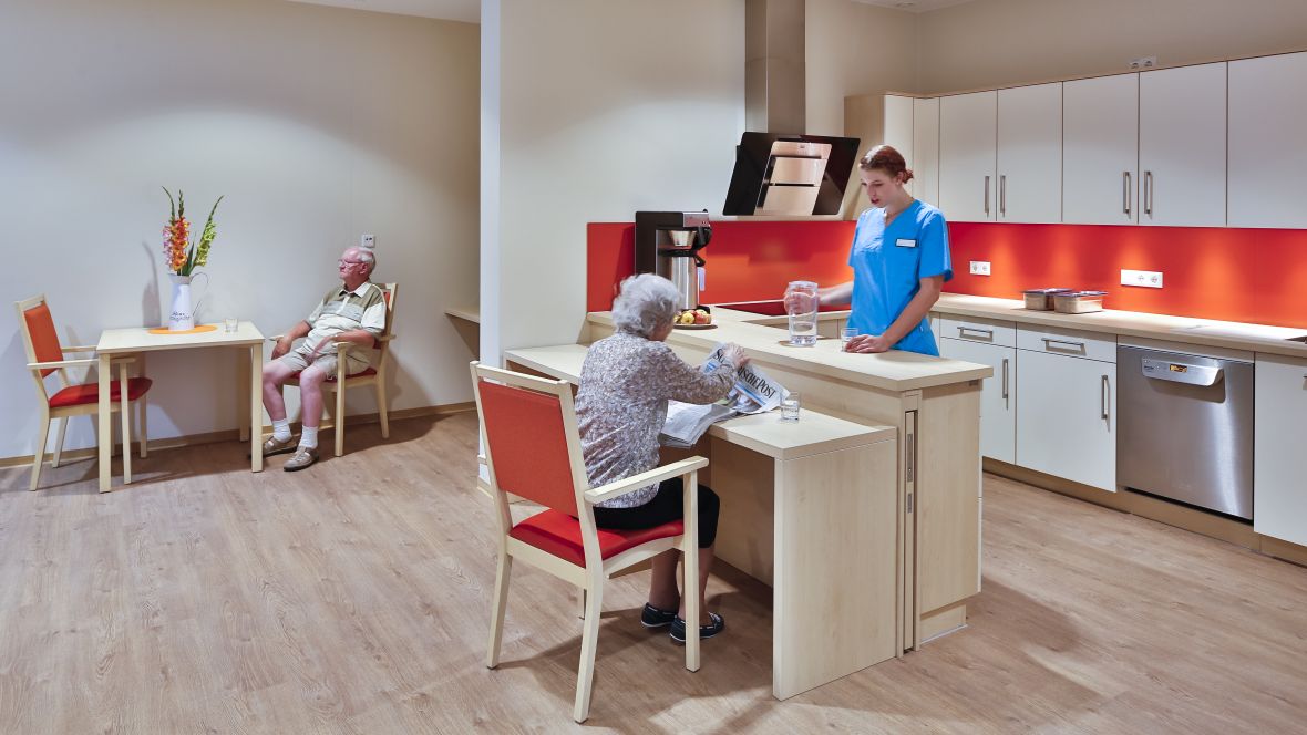Wohnen und Pflegen im Sonnengarten Senioren und Pflegerin in Küche – Forbo Allura Wood