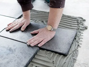 Hände beim Platten verlegen mit Forbo Eurocol zementbasiertem Bauklebstoff für Fliesen.
