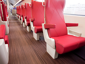 Transport: Ausschnitt aus einem Eisenbahnwagen mit dunklem gestreiften Forbo Boden Marmoleum Striato und roten Sitzplätzen.